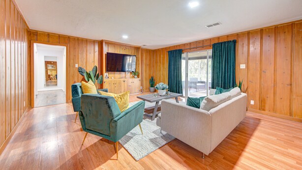 A spacious living room with wooden walls, a sofa, a chair, a TV, and a dining area. - Workers Haven - Pet Friendly- Patio - Fiber Wi-Fi - King Bed (Beaumont)