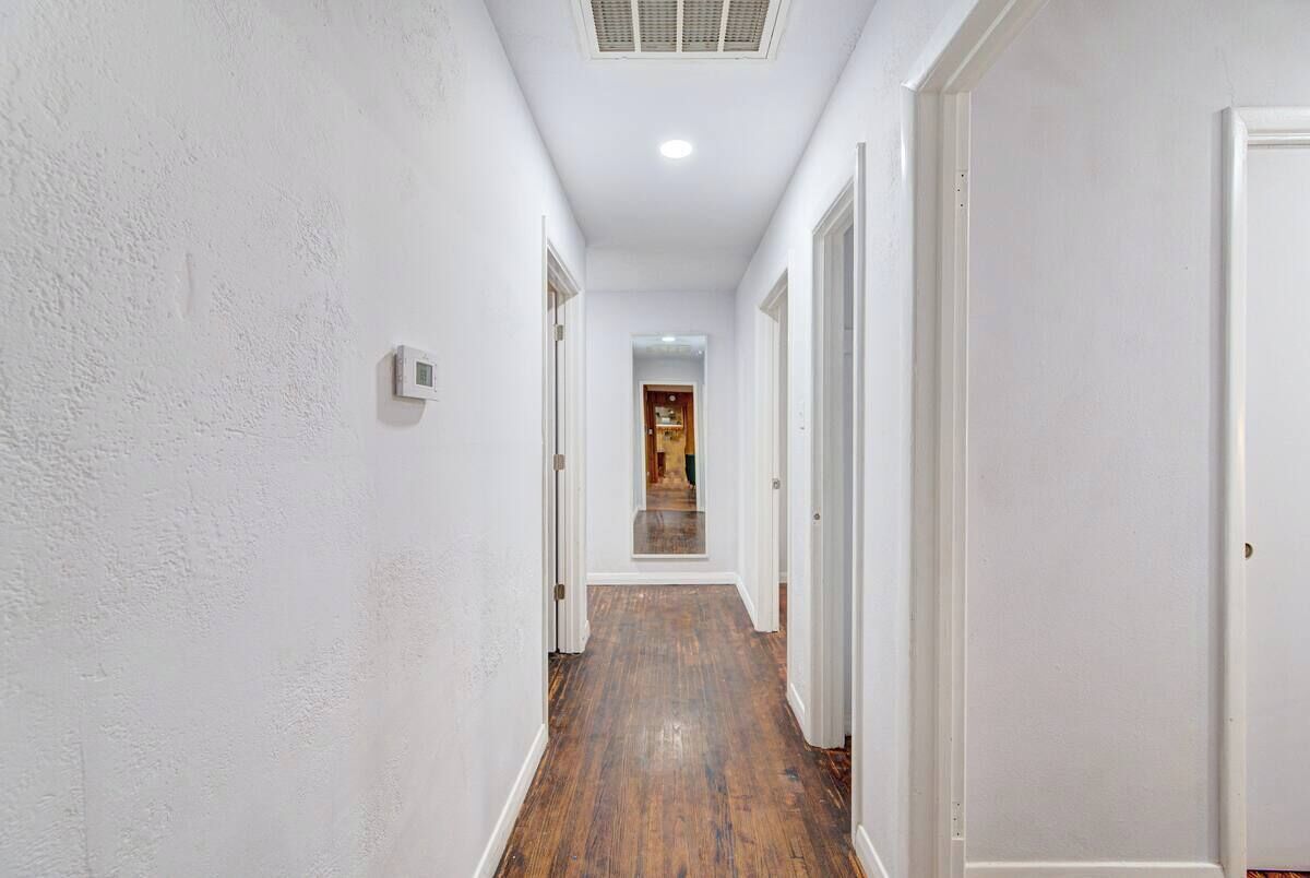 Un corridoio stretto con pareti bianche e pavimento in legno, che conduce a una porta in fondo.
