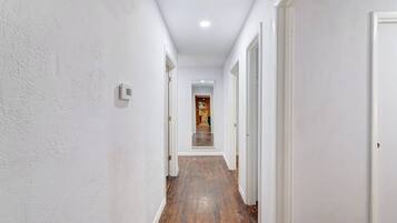 Un corridoio stretto con pareti bianche e pavimento in legno, che conduce a una porta in fondo.