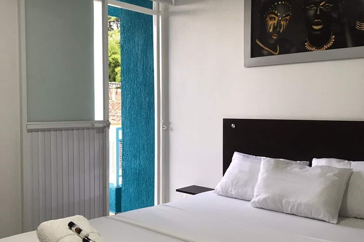 Ein Hotelzimmer mit einem Bett, weißen Kissen, einem schwarzen Kopfteil, einem Nachttisch, einem Handtuch und einer Flasche sowie einem Bild an der Wand.