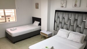 A hotel room with two single beds, a larger bed, a small bedside table, and a window with a view.