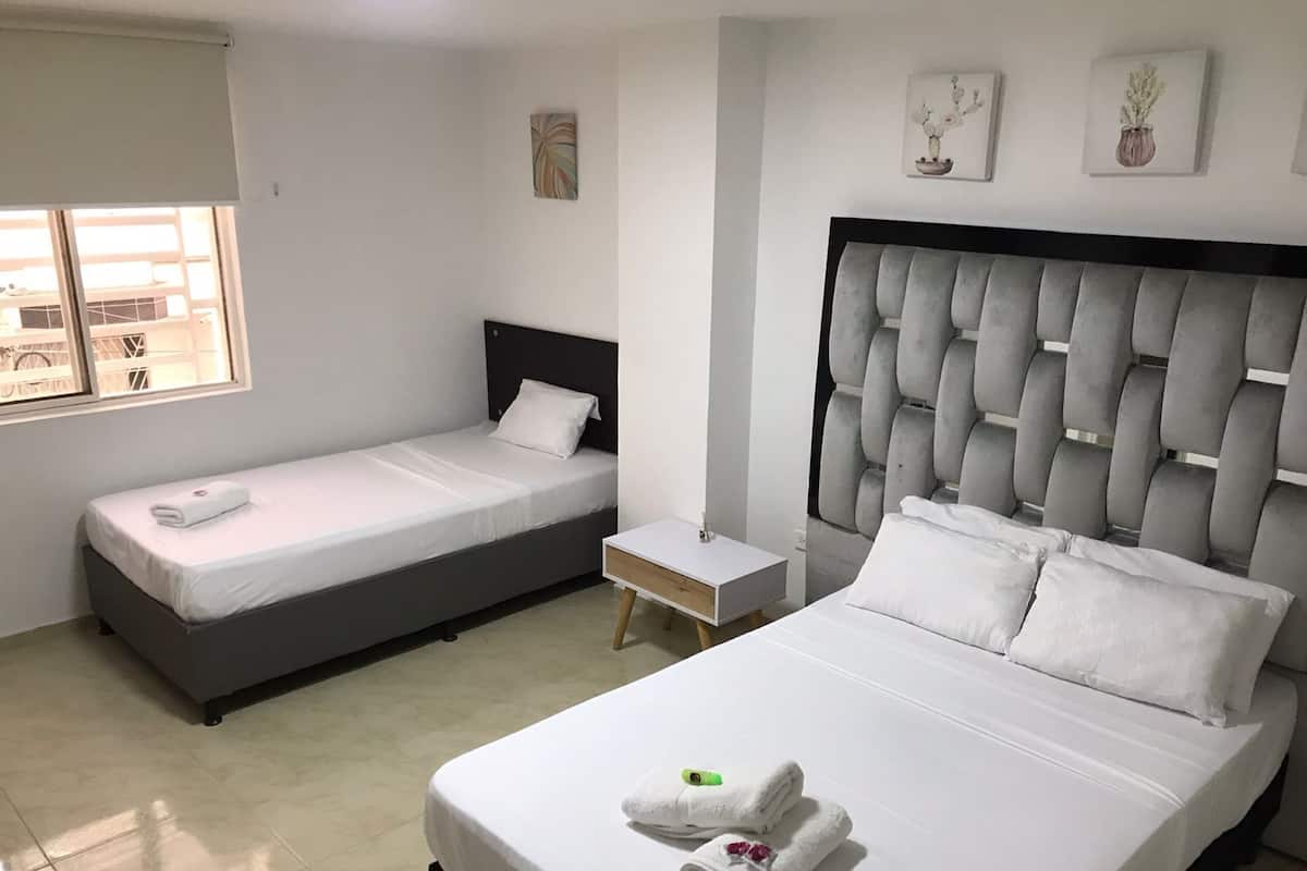 Ein Hotelzimmer mit zwei Einzelbetten, einem größeren Bett, einem kleinen Nachttisch und einem Fenster mit Blick.