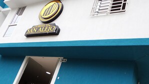 A hotel entrance with a blue and white facade, a prominent logo, and a sign reading "HOTEL SAN ALEJO".