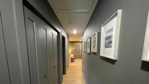 Un pasillo con paredes grises, piso de madera y una serie de puertas a un lado.