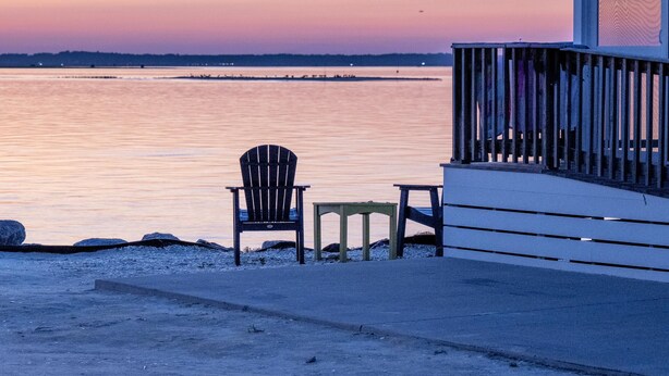 Vista de la playa con una terraza de madera, una silla y una mesa.