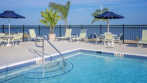 Zona de piscina con sillones de descanso y sombrillas, una piscina con indicador de profundidad y vista al mar.