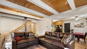 A spacious living area with a large brown leather sectional sofa, a fur rug, and a wooden ceiling.