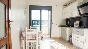 Une cuisine avec des meubles blancs, une table à manger recouverte d’une nappe rose et une vue sur le balcon extérieur.