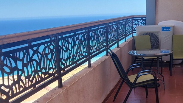 Une terrasse offrant une vue sur l’océan, comprenant une table et des chaises, une rambarde décorative et un appareil de climatisation.