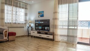 Un salon avec un plancher en bois, un canap é, un téléviseur posé sur un meuble et un balcon doté d’une balustrade.