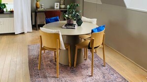 A dining area with a round table, four chairs, a rug, and a window with a view of buildings. - Main Street Beach apartment 150 meters from the beach  (Noordwijk)