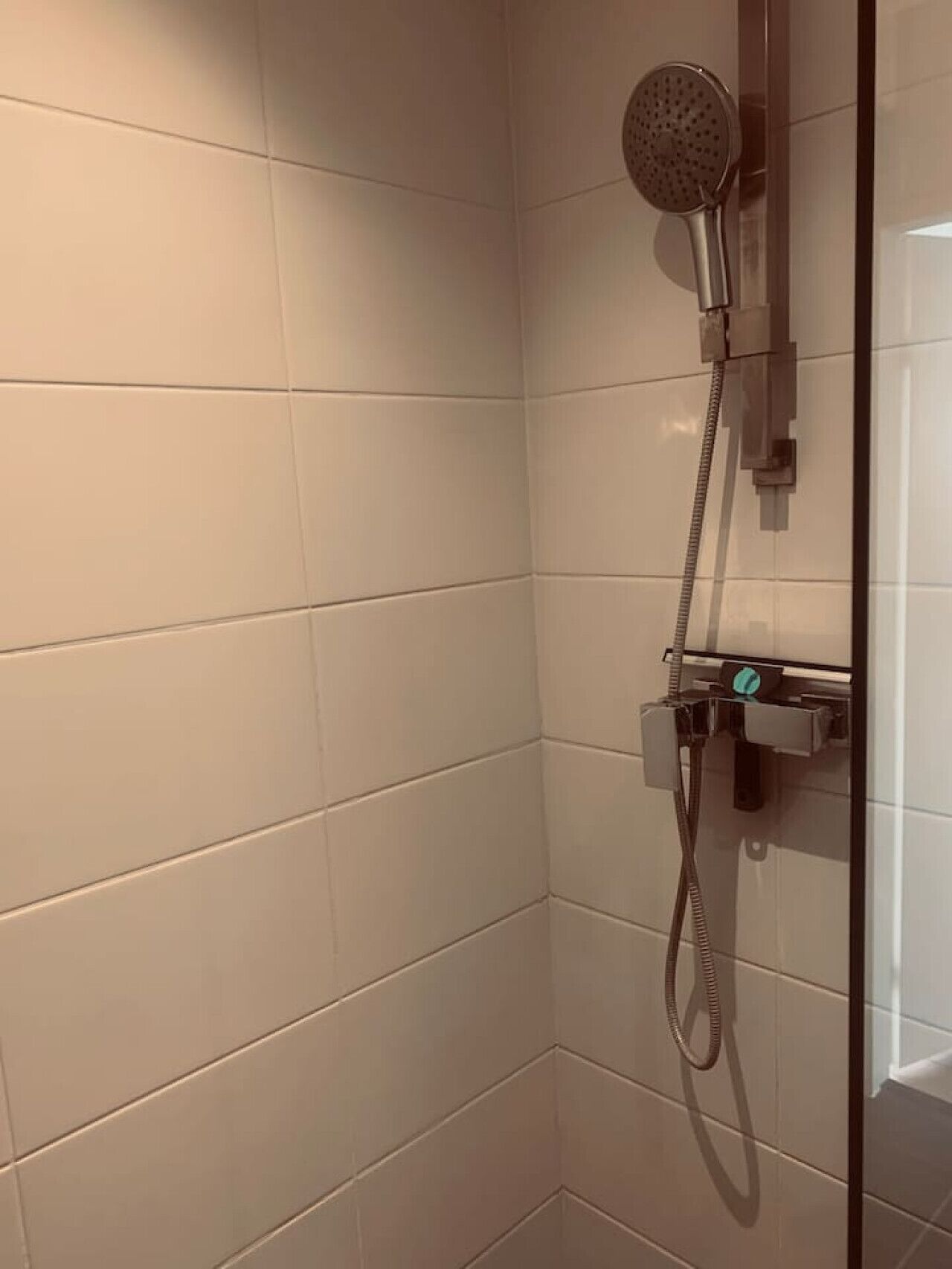 A corner of a bathroom with white tiled walls and a shower with a handheld showerhead.