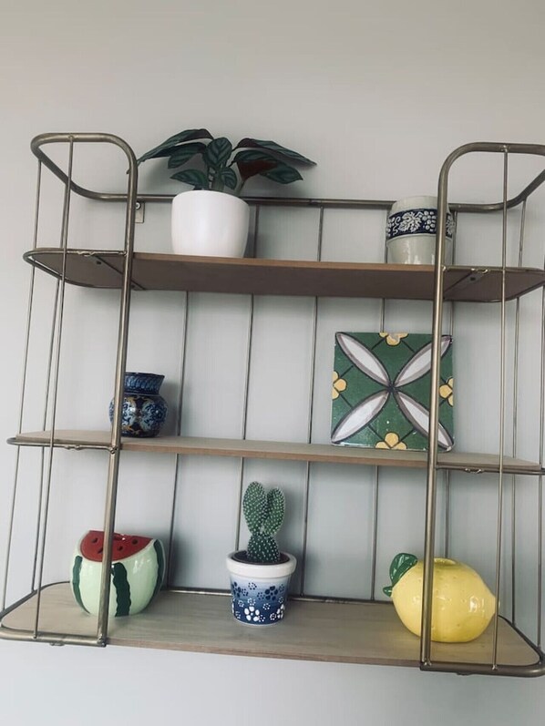 Une étagère en métal ornée de divers objets décoratifs, notamment un pot de fleurs, un cactus et un récipient en forme de fruit.