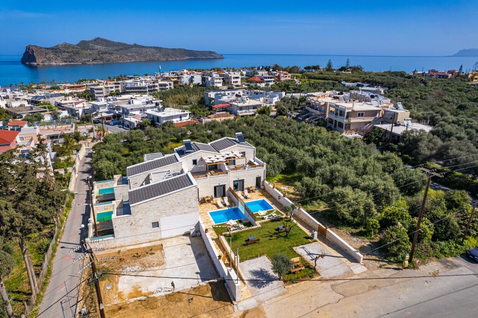 A modern villa with a swimming pool, surrounded by lush greenery and a view of the sea.