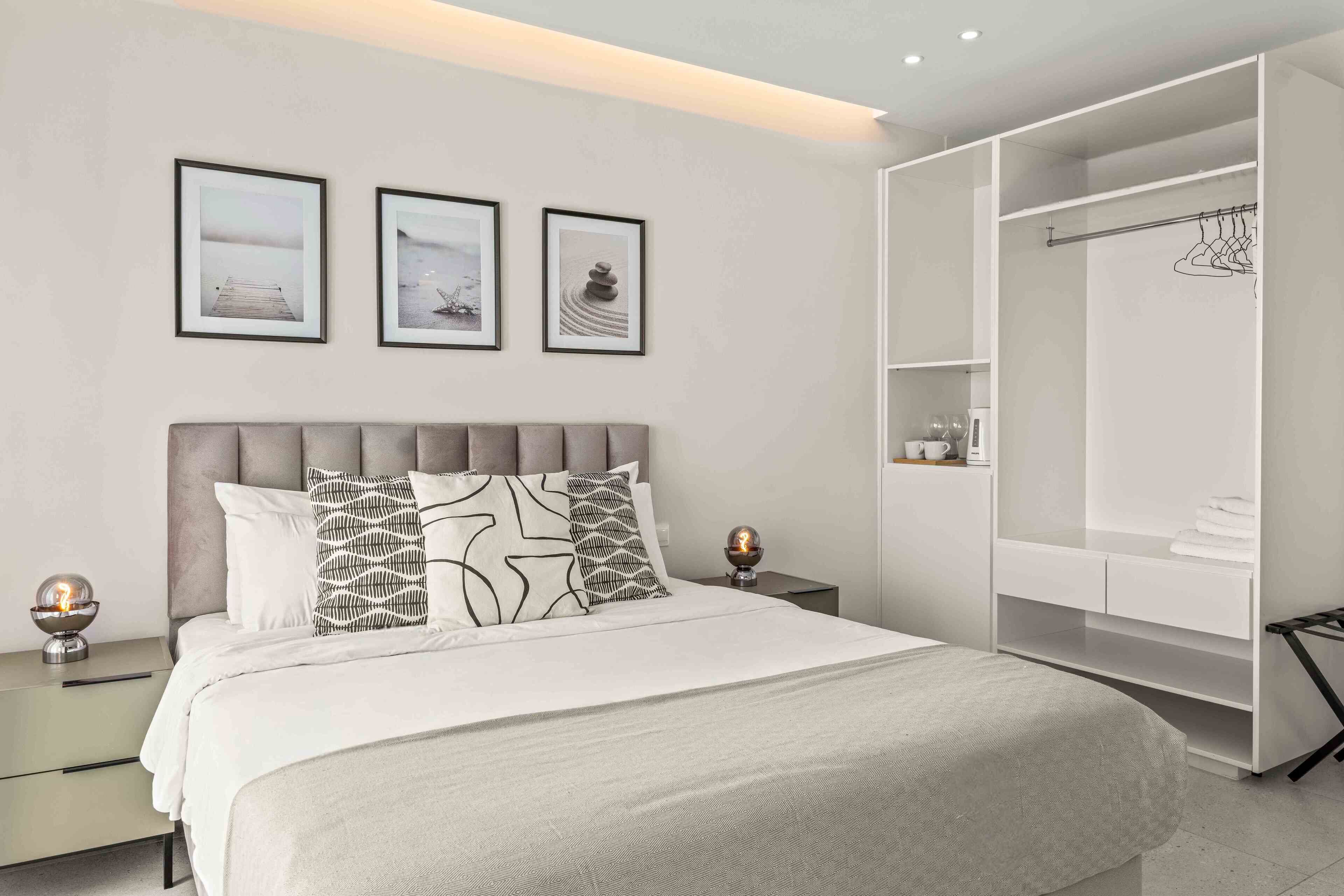 Un dormitorio moderno con una cama grande, un vestidor y tres cuadros en la pared.