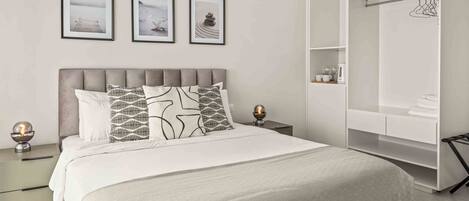Un dormitorio moderno con una cama grande, un vestidor y tres cuadros en la pared.