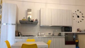 Une cuisine moderne avec des meubles blancs, un four à micro-ondes et un four traditionnel. On y trouve une table à manger avec des chaises jaunes.