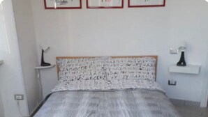 Une chambre à coucher avec un lit, deux poufs rouges, une table de chevet, une lampe et des tableaux encadrés accrochés au mur.