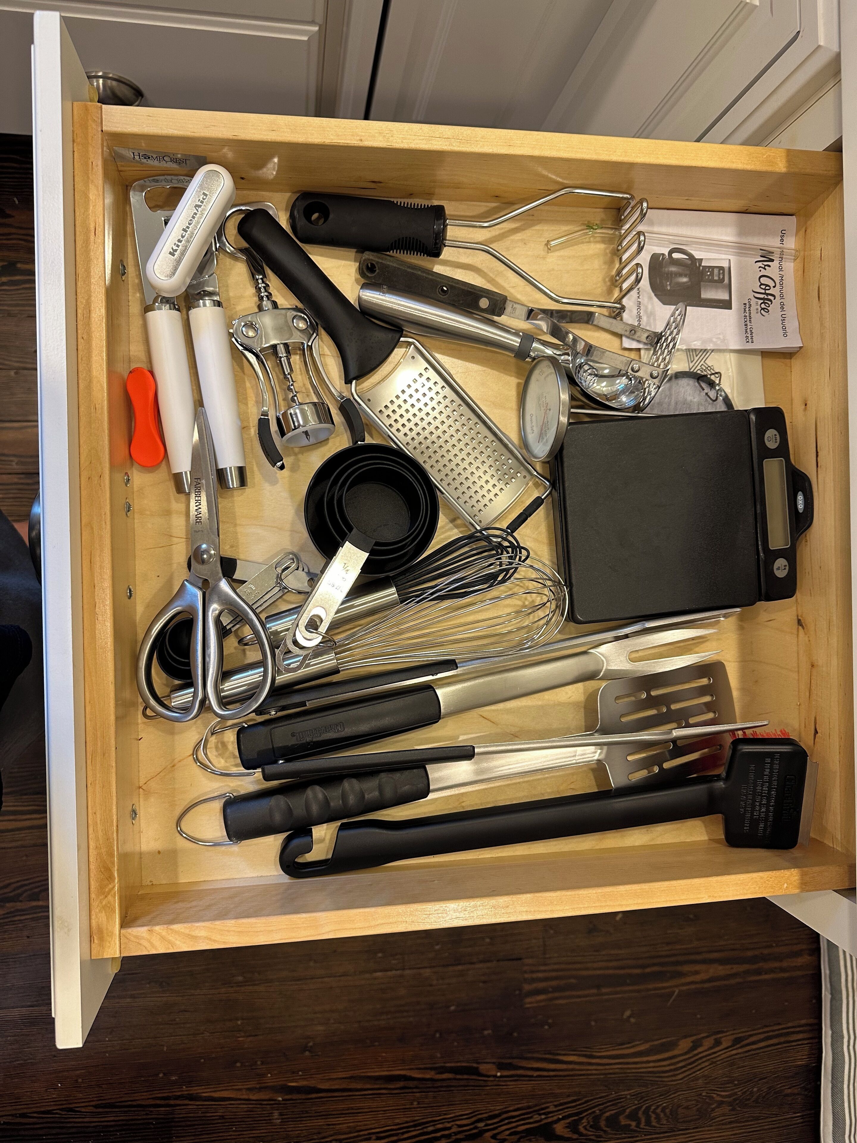 A drawer containing various kitchen utensils and tools, including a grater, whisk, and scissors.