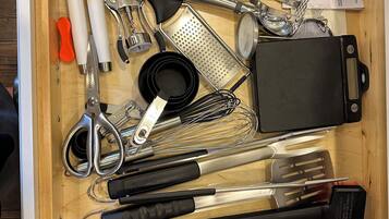 A drawer containing various kitchen utensils and tools, including a grater, whisk, and scissors.