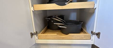 A kitchen cabinet with two shelves, each holding pots and pans.