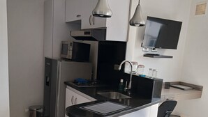 A modern kitchen with white cabinets, a black countertop, stainless steel appliances, and two black bar stools. - 506 Moderno Aparta-Suite en Versalles Tipo Loft - Cali Tower Suites & Lofts (Cali)