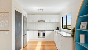 Een moderne keuken met witte kasten, roestvrijstalen apparatuur en uitzicht op het platteland door een groot raam.