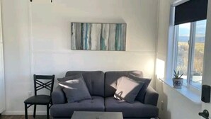 Ein modernes Wohnzimmer mit einem dunkelgrauen Sofa, einem schwarzen Sessel, einem kleinen Couchtisch und einem Deckenventilator.