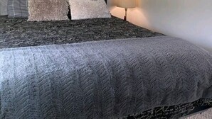 Ein Schlafzimmer mit einem Bett, Kissen, einem Deckenventilator, einer Wandleuchte und einem Gemälde.