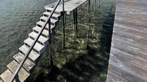 A wooden pier extending into clear turquoise water, with a staircase leading down to the water's edge.