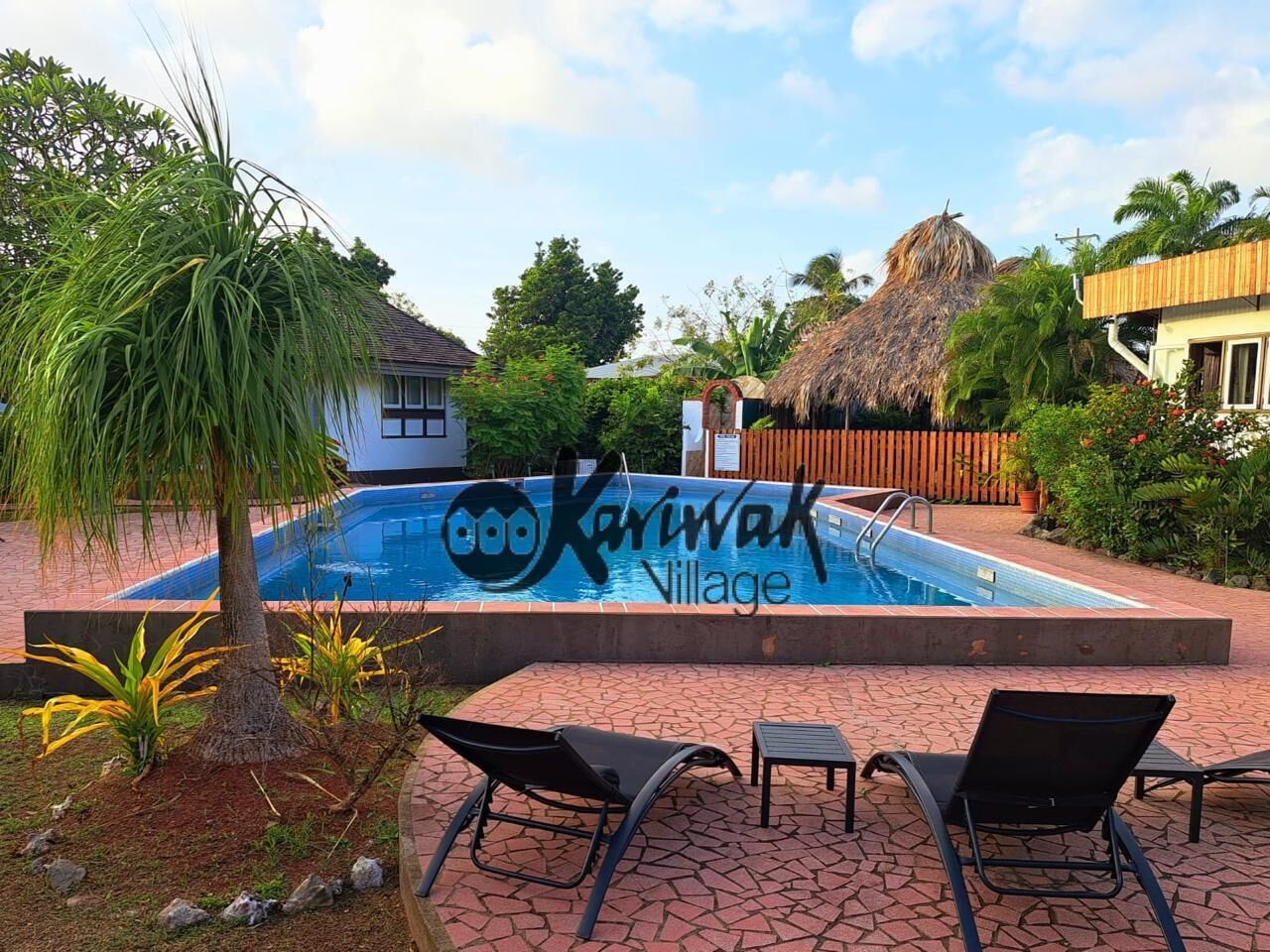 A swimming pool with lounge chairs, surrounded by tropical vegetation and a wooden fence.