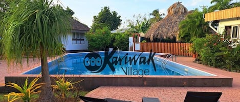 A swimming pool with lounge chairs, surrounded by tropical vegetation and a wooden fence.
