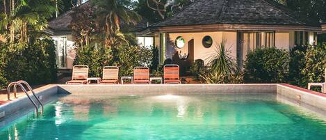A swimming pool with lounge chairs and a small building with a thatched roof.