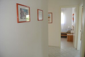 A hallway with framed pictures on the wall, leading to a bedroom with a bed and a nightstand. - Spacious Flat With Terrace in Lignano Pineta (Lignano Sabbiadoro)