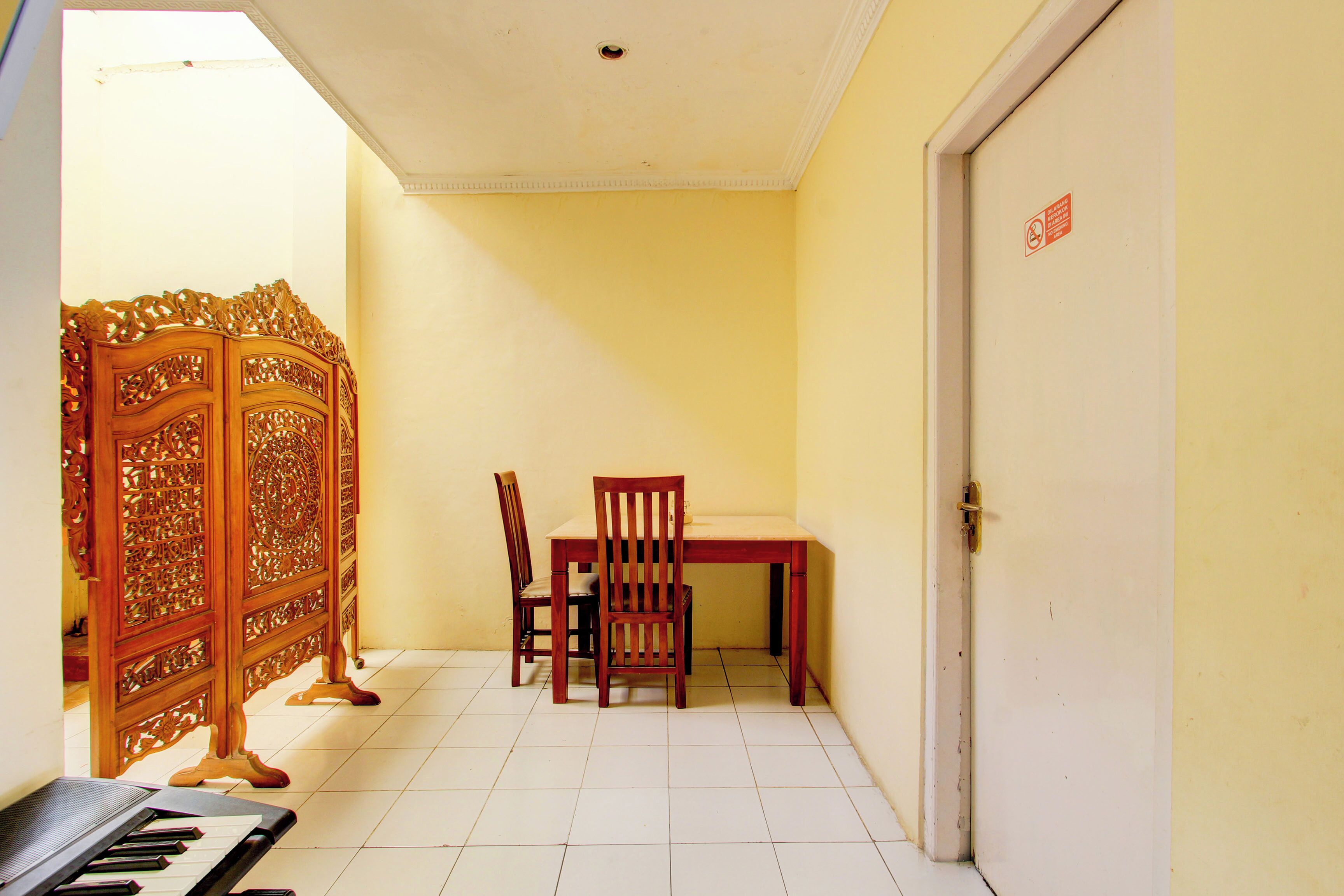 A room with a piano, a wooden cabinet, a table with chairs, and a door with a sign.