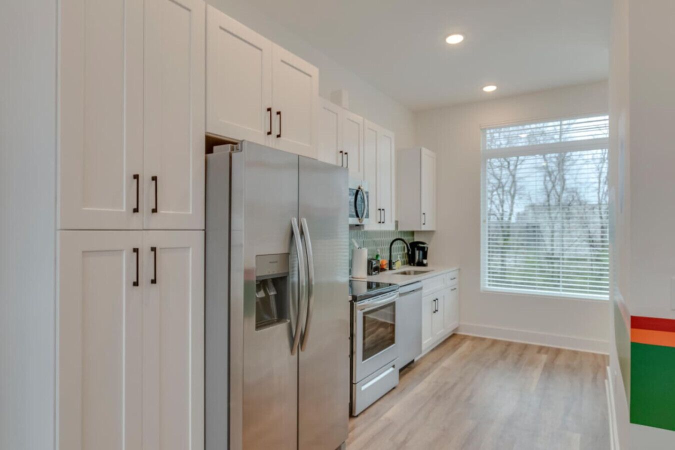 A modern kitchen with white cabinets, stainless steel appliances, and a large window providing natural light.