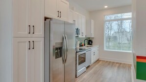 Una cocina moderna con armarios blancos, electrodomésticos de acero inoxidable y un amplio ventanal que proporciona luz natural.