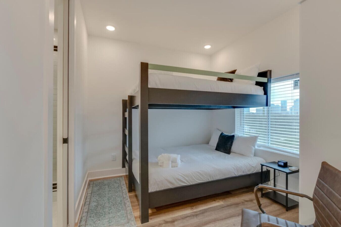 A bunk bed room with a window, a bedside table, and a chair.