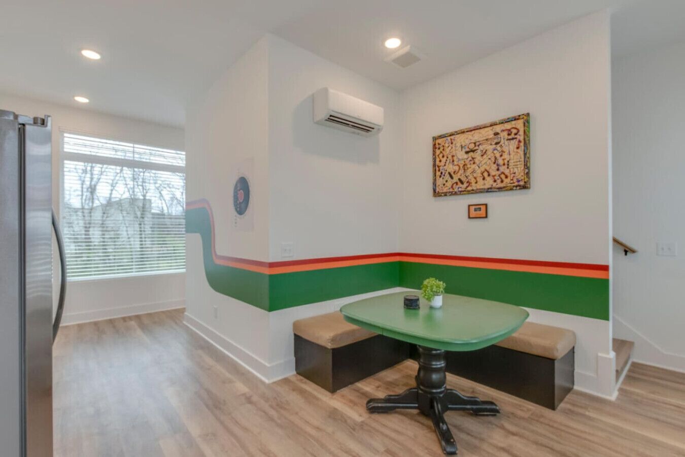 A modern kitchen with a built-in refrigerator, a dining table with benches, and a colorful accent wall.