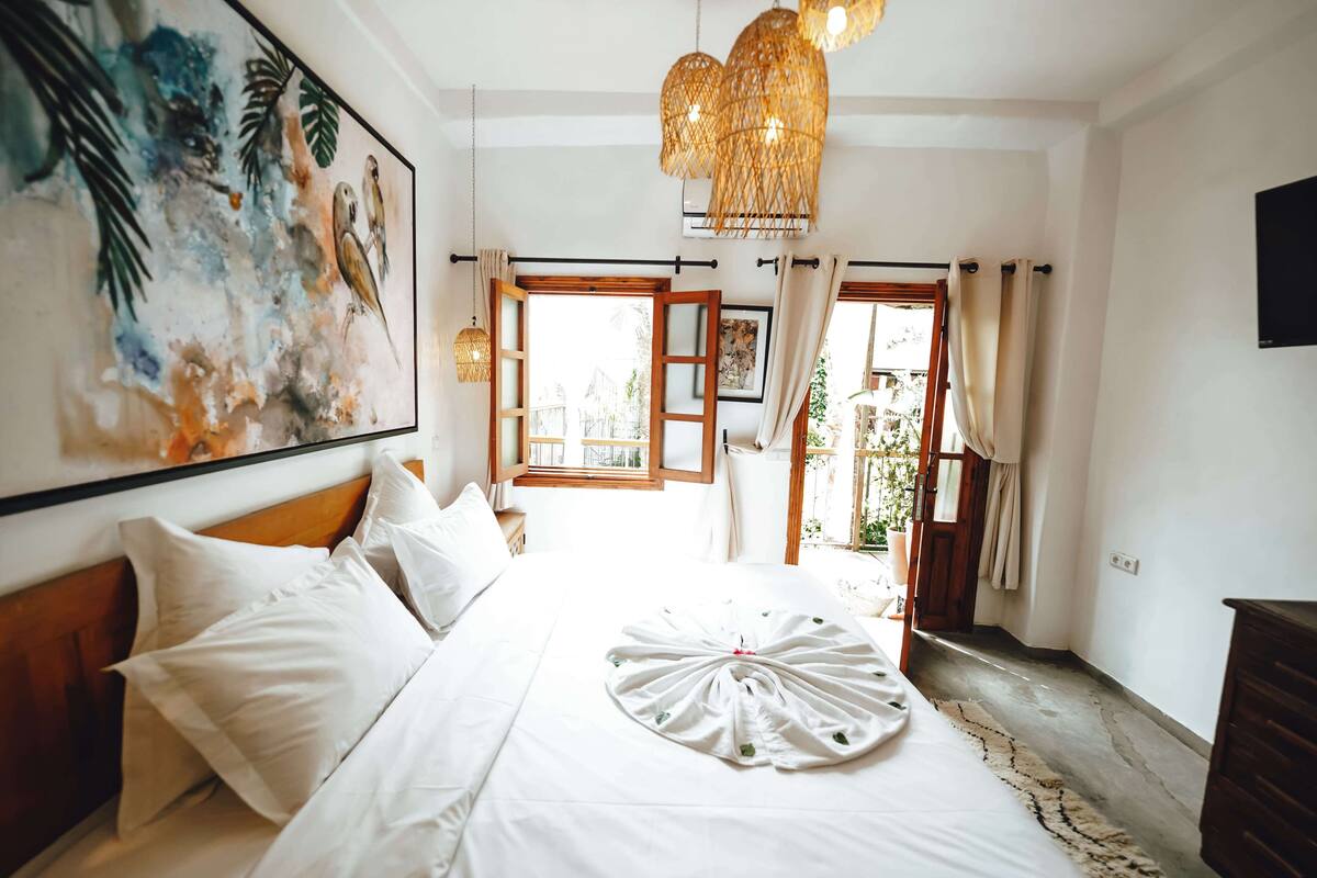 A hotel room with a large bed, a painting on the wall, and a view of the outdoors.
