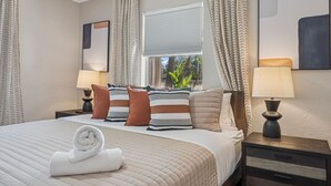 A hotel room with a large bed, two bedside tables, a window with curtains, and a view of greenery outside. - Modern Pool Home, Central to Beach and Downtown (Seminole)