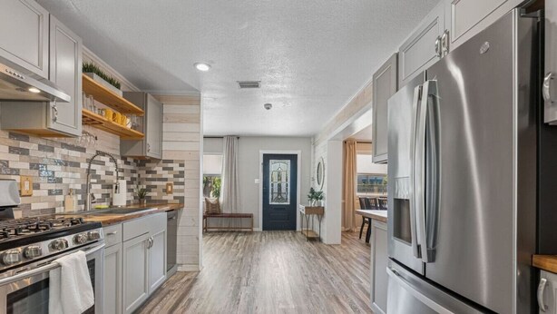 A modern kitchen with stainless steel appliances, a tiled backsplash, and wooden flooring. - Modern Pool Home, Central to Beach and Downtown (Seminole)