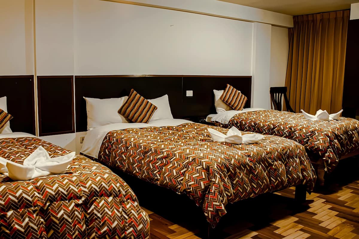 A hotel room with three beds, each with a patterned bedspread and pillows.