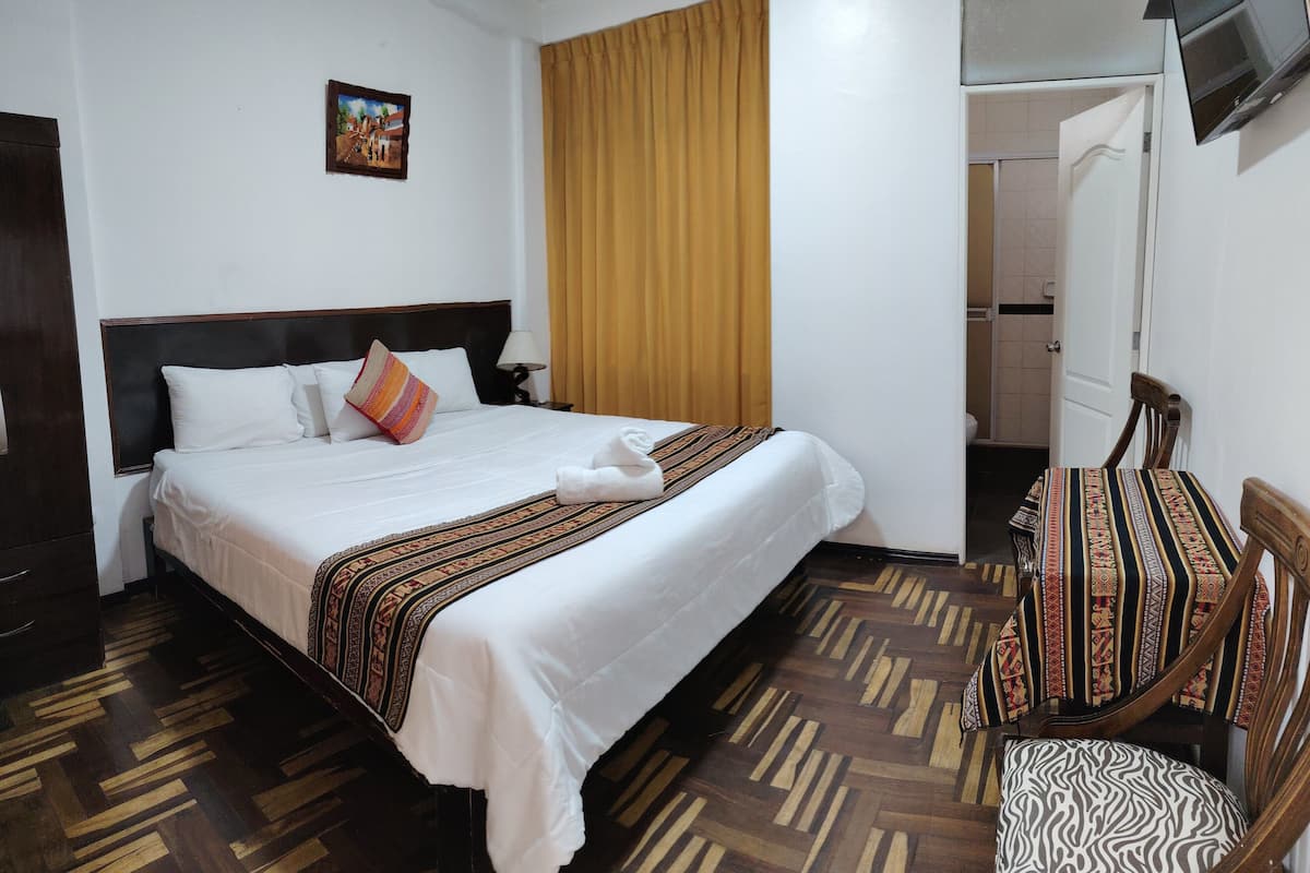 A hotel room with a bed, a chair, a television, and a door leading to a bathroom.