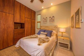 A bedroom with a bed, wooden wardrobe, bedside table, lamp, and wall art. - 3BD Begati Ocean View Pool Beach Resort (San José del Cabo)