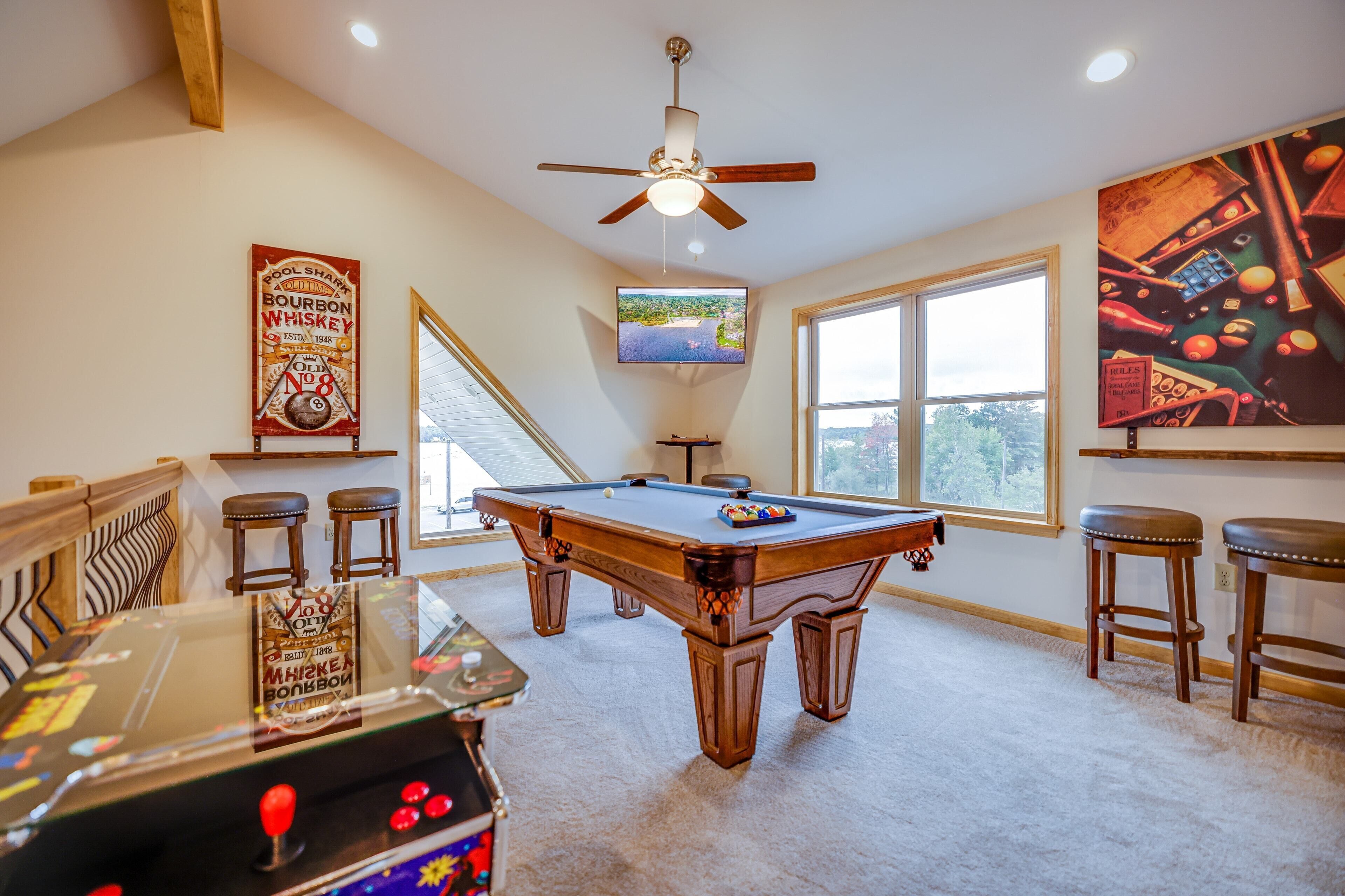 A pool table in a room with a ceiling fan, a television, and a window with a view.