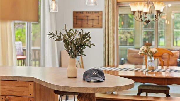 Un coin repas avec une table en bois, un vase agrémenté de plantes et un chapeau posé sur la table.