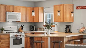 Une cuisine avec des meubles en bois, un micro-ondes blanc, une cuisinière et une machine à café.