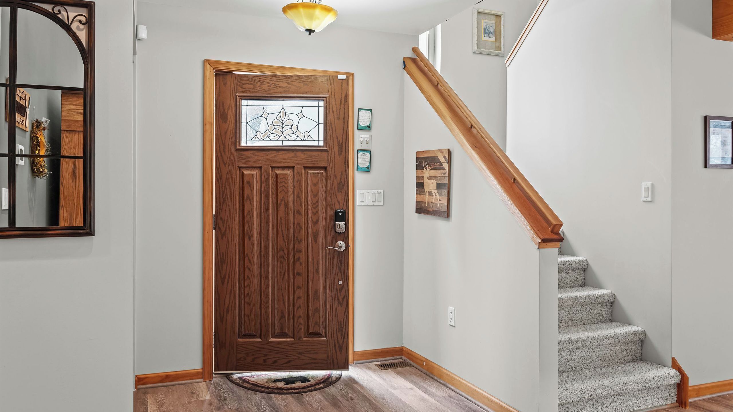 Una puerta principal de madera con un panel de vidrio, una escalera con barandillas de madera y un candelabro en lo alto.
