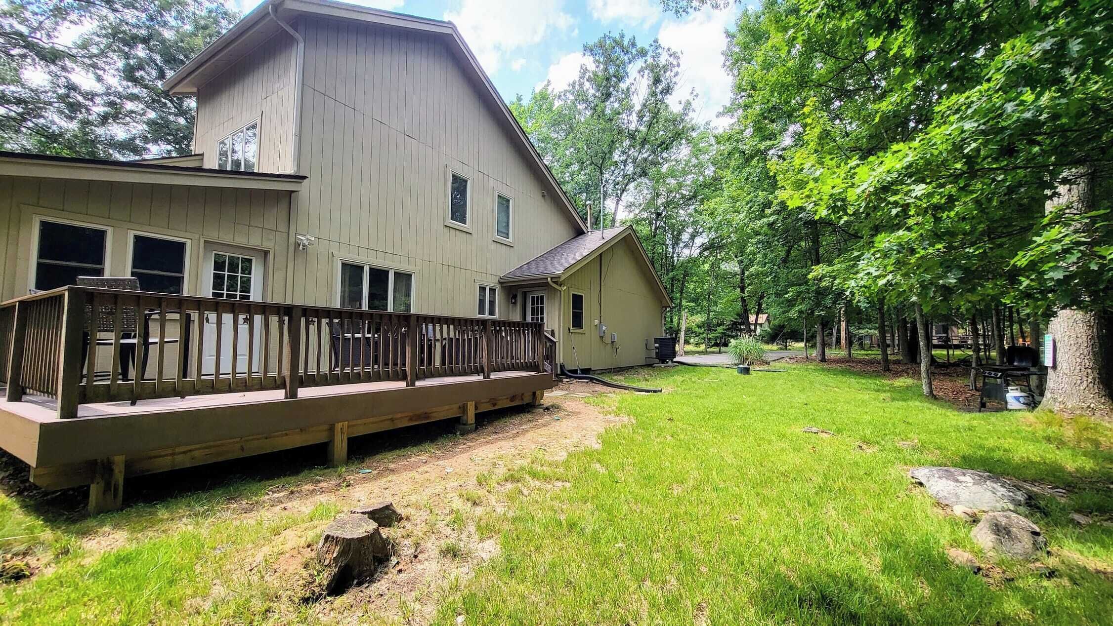 A two-story house with a deck, surrounded by a grassy yard and trees.
